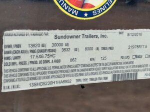 A close-up of a vehicle information sticker for Sundowner Trailers, Inc., showing weight ratings, tire size, pressure, and VIN details. The label is affixed to a metallic surface—ideal for Stock Trailers and Custom Show Trailers. -Stillwater Trailer Sales