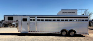 A large silver Elite 6 Horse livestock trailer with multiple vents, two axles, and a gooseneck hitch is parked on a gravel lot under a clear sky; Elite Trailers branding and Tack #23223 are displayed on the upper section. -Stillwater Trailer Sales