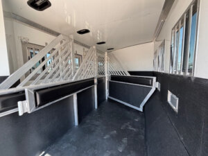 Interior of a Bloomer 4H horse trailer with metal dividers forming separate stalls, padded walls, non-slip black flooring, and barred windows for ventilation. The space is clean and well-lit&mdash;ideal for any horse trainer. -Stillwater Trailer Sales