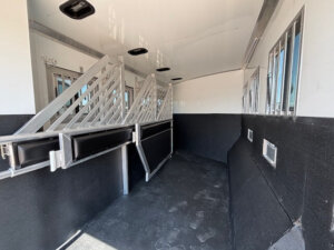 Interior of a Bloomer horse trailer with padded dividers, black flooring, and windows with metal bars along the walls, designed to safely transport multiple horses. Ideal for riders or those seeking a 4H Trainer setup. -Stillwater Trailer Sales