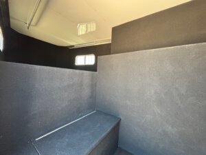 A view of the interior of a horse trailer, showing black padded walls, a bench-like platform, and two small rectangular windows letting in natural light—perfect for those seeking new and used trailers with Living Quarters custom options. -Stillwater Trailer Sales
