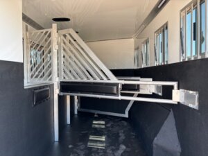 Interior of a horse trailer featuring metal dividers, padded panels, and barred windows along the side. The textured floor and black protective walls add comfort—ideal for Stock Trailers or those seeking new and used trailers with premium features. -Stillwater Trailer Sales