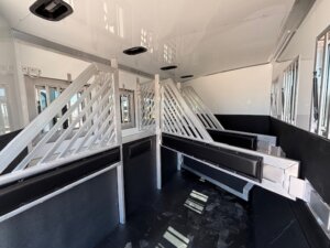 The image shows the interior of a horse trailer from a reputable horse and livestock trailer sales provider, featuring metal dividers, padded walls, open windows, and durable flooring for safely transporting multiple horses. -Stillwater Trailer Sales