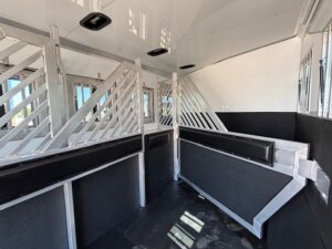 Interior of a horse trailer featuring metal stall dividers, padded walls, and black rubber flooring. This clean, well-lit space resembles custom show trailers, with vents and windows providing a comfortable environment for your horses. -Stillwater Trailer Sales