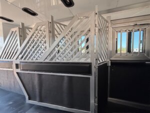Interior of a horse trailer with metal dividers and bars, designed to safely separate and secure animals during transport. Perfect for those seeking custom show trailers or exploring new and used trailers at leading trailer sales. Clean, well-lit, with black padded walls. -Stillwater Trailer Sales