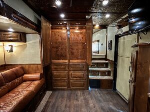 A warmly lit room with dark wood floors, built-in wooden cabinets, and a brown leather sofa on the left shows off the luxury found in Living Quarters custom spaces—perfect for those seeking comfort like that in new and used trailers. -Stillwater Trailer Sales