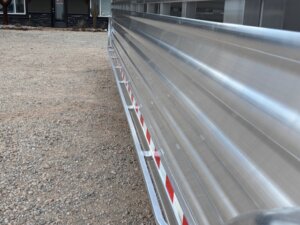 Close-up side view of a metallic Stock Trailer with red and white reflective tape, parked on a gravel surface near a building—showcasing quality construction perfect for custom show trailers or living quarters custom designs. -Stillwater Trailer Sales