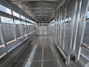 Interior view of an empty, metal livestock trailer with grated flooring and side ventilation panels, photographed in daylight. This clean, well-lit model highlights quality construction offered through our new and used trailers and custom show trailers. -Stillwater Trailer Sales