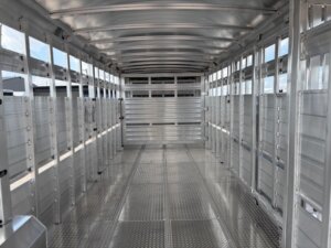 Interior view of an empty aluminum livestock trailer with ribbed walls and diamond plate floor—perfect for horse and livestock trailer sales or converting into Custom Show Trailers with Living Quarters custom features. Light filters in through open slatted sides. -Stillwater Trailer Sales