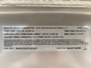 A manufacturer label on a trailer for horse and livestock trailer sales displays specs like weight, tire size, and pressure. Details include VIN, manufacturer name, date, axle weight, rim size, and compliance statements in English and French. -Stillwater Trailer Sales