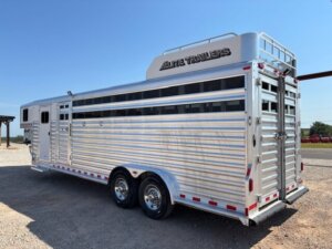An Elite 26 Stock Combo livestock trailer with two axles, ribbed metal sides, rear and side doors, ventilation slats, and Elite Trailers branding on the upper storage compartment sits parked on gravel under a clear blue sky. -Stillwater Trailer Sales