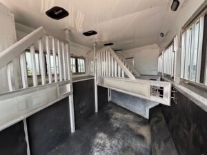 Interior of an empty horse trailer featuring metal dividers, windows with bars along the sides, non-slip black flooring, and white walls and ceiling. Explore our Custom Show Trailers designed for transporting multiple horses in comfort. -Stillwater Trailer Sales