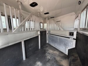 Interior of an empty horse and livestock trailer with metal dividers and windows. The dark floor shows slight wear, while clean metal panels line the walls. Ample light streams in from ceiling vents and windows—perfect for New and used trailers or Custom Show Trailers. -Stillwater Trailer Sales