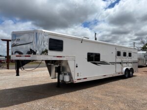 A large white gooseneck horse and livestock trailer with black accents is parked on a gravel lot under a partly cloudy sky. This Custom Show Trailer features multiple windows, side vents, and dual axles—perfect for horse and livestock trailer sales. -Stillwater Trailer Sales