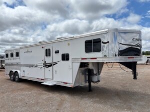 A large white gooseneck horse trailer with multiple windows and black accent stripes is parked on a gravel lot under a cloudy sky—an ideal choice for those seeking new and used trailers or expert horse and livestock trailer sales. -Stillwater Trailer Sales