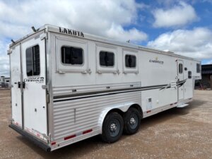 A white Lakota Charger horse trailer with three windows on the side, dual axles, and silver accents is parked on gravel under a partly cloudy sky—perfect for those seeking Living Quarters custom options. -Stillwater Trailer Sales