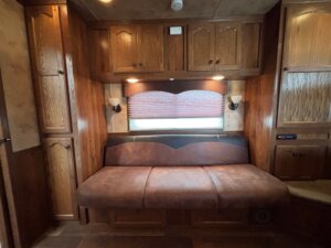 A brown leather couch sits against a wooden wall with upper cabinets, two sconces, and a window with a closed brown blind—perfect for relaxing after browsing new and used trailers or designing your custom show trailers with living quarters. -Stillwater Trailer Sales