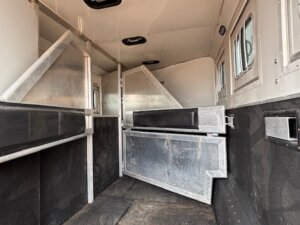 The interior of this horse trailer is clean and well-maintained, featuring metal partitions, padded dividers, windows on the right side, and black rubber flooring—a great example of the quality found in our new and used trailers. -Stillwater Trailer Sales