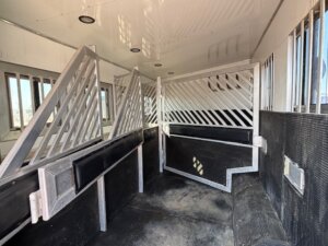 Interior of a horse trailer with divided stalls, metal gates, rubber floor mats, barred windows, and overhead lights. Perfect for safe transport—explore our horse and livestock trailer sales for new and used trailers just like this. -Stillwater Trailer Sales
