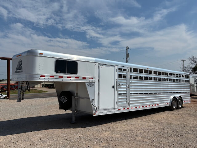 An Elite 32 Combo large silver gooseneck livestock trailer with multiple side vents and rear double axles is parked on a gravel lot under a partly cloudy sky. -Stillwater Trailer Sales