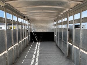 Interior of an empty Elite 32' Combo livestock trailer with a curved roof, grated side vents, and textured flooring, parked outdoors on a sunny day. -Stillwater Trailer Sales