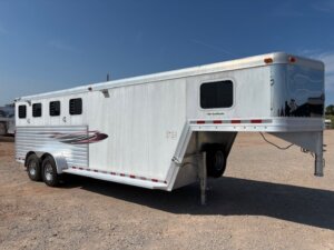 A silver Dream Coach gooseneck horse trailer with three windows and red and black decals is parked on a gravel lot under a clear blue sky. Perfect for transporting up to 4 horses in style and comfort. -Stillwater Trailer Sales
