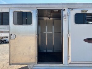 Open door of an empty silver Dream Coach horse trailer, showing a metal interior with vertical support beams. Part of another 4 Horse trailer is visible in the background outside. -Stillwater Trailer Sales