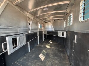 The interior of this 4 Horse Dream Coach horse trailer features metal dividers, barred windows, a non-slip floor, and a skylight. Sunlight streams through the windows, casting soft shadows across the spacious floor. -Stillwater Trailer Sales