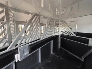 Interior of a Signature 5 Horse Bloomer trailer with metal dividers, padded walls, and gated stalls. The well-lit space is clean and offers several sections for safe animal transport. -Stillwater Trailer Sales