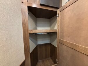 An open wooden closet inside the SMC 1706, 14' horse trailer features two shelves and a hanging rod, with an empty interior lined with light-colored paneling. The door is open, revealing the spacious storage area within. -Stillwater Trailer Sales