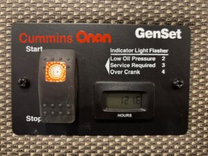 A Cummins Onan GenSet control panel, ideal for an SMC horse trailer, features a lit orange indicator, digital display reading 1216 hours, and a legend showing codes for low oil pressure, service required, and over crank. -Stillwater Trailer Sales