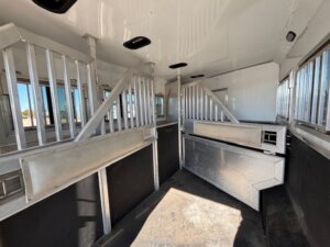Interior of a 1706 SMC 4 Horse trailer featuring metal dividers, black lower walls, and white upper walls and ceiling. The 14' horse trailer includes windows along the left side and ventilation openings in the ceiling. -Stillwater Trailer Sales