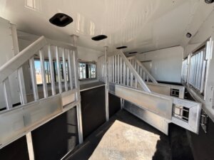 Interior of a clean, empty SMC 4 Horse trailer with metal dividers, barred partitions, and rubber flooring, designed for transporting multiple horses. Sunlight streams through the windows in this spacious 14' trailer. -Stillwater Trailer Sales
