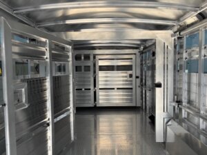 Interior view of an empty Elite 30' combo livestock trailer with metal walls, gates, and a textured floor, featuring several compartments and open-air slots for ventilation—ideal for transporting show cattle. -Stillwater Trailer Sales