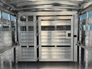 Interior view of an empty Elite 30 livestock trailer, showing metal gates and secure latches, with light reflecting off the polished surfaces—ideal for transporting show cattle or as a versatile Cattle Combo setup. -Stillwater Trailer Sales