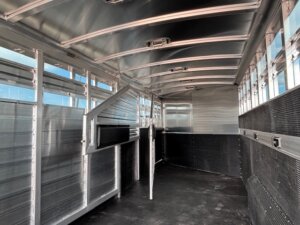 Interior view of an empty Elite 24' Stock Combo trailer with metal walls, ceiling supports, and rubberized flooring. The trailer is clean and well-lit, featuring gates and ventilation slats along the sides. -Stillwater Trailer Sales