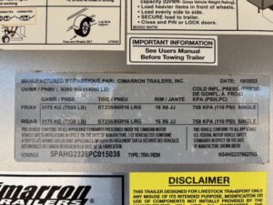 Close-up of a Cimarron trailer information sticker showing manufacturer details, load limits, and specs for a 4 Horse Trainer. Text appears in English and French, with safety warnings and a serial number at the bottom. -Stillwater Trailer Sales