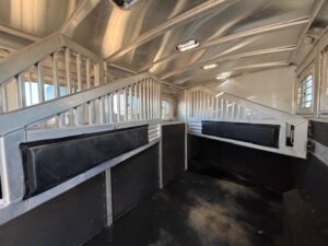 Interior of an empty Elite 4 Horse Trailer with padded dividers, metal bars, and clean black flooring for safe animal transport. The metallic walls and ceiling are well-maintained, and a finished dressing room adds extra convenience. -Stillwater Trailer Sales