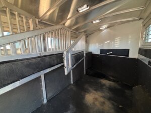 Interior of an empty Elite 4 Horse trailer with metal dividers, padded walls, and ceiling lights. The worn floor and finished dressing room highlight its design focused on safe, comfortable animal transport. -Stillwater Trailer Sales