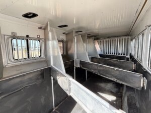 Interior of a 6 Horse Sundowner trailer with several individual stalls separated by metal partitions, metal bars on the windows, and a clean, well-lit environment. -Stillwater Trailer Sales
