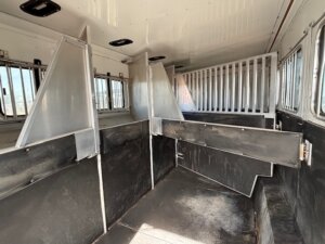 The interior of this Sundowner 6 horse trailer features divided stalls, metal partitions, barred gates, and side windows, all designed for safely transporting multiple horses. -Stillwater Trailer Sales