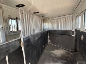 Interior of a 6 Horse Sundowner horse trailer with metal dividers and barred windows, featuring black padded walls and a slightly dirty floor. -Stillwater Trailer Sales