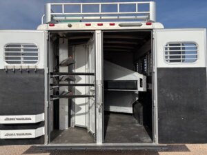The open rear doors of this Elite 3 Horse Trailer reveal saddle racks on the left and an empty horse stall area inside. Ventilation windows and metal bars are built into the doors, perfect for any Outback LQ adventure. -Stillwater Trailer Sales