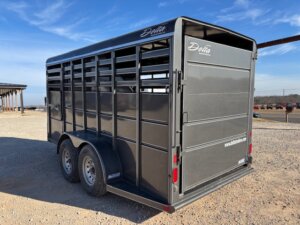 A black, enclosed livestock trailer with two axles is parked on gravel. The trailer has vertical ventilation slats, rear double doors, and &ldquo;Delta&rdquo; branding on the upper side and back. Blue sky is visible in the background. -Stillwater Trailer Sales