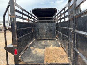 The interior of a Travalong 16' Half Top Stock trailer with metal sides, a rubber mat on the floor, and a wooden section near the entrance, photographed from the open rear gate. -Stillwater Trailer Sales