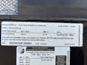 A close-up of two labels on a Travalong 16' Stock Trailer. The top label lists manufacturing details, weights, tire specifications, and compliance information, while the lower label provides tire and loading info in English and French for this Half Top Stock model. -Stillwater Trailer Sales
