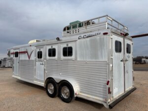 A large silver C&C 3 horse trailer with three windows and two doors on the side is parked on gravel. It features dual axles, a roof rack with equipment secured on top, and C&C Trailers branding, offering spacious living quarters inside. -Stillwater Trailer Sales
