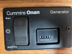 Close-up of a Cummins Onan Generator control panel with start switch and hour meter reading 4520.1, mounted on the wooden surface of a 2001 Bloomer 3 horse trailer. -Stillwater Trailer Sales