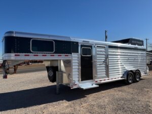 An Elite 4+1 Combo silver and black gooseneck livestock trailer with Side Tack and two axles is parked on gravel in an outdoor lot under a clear blue sky. -Stillwater Trailer Sales