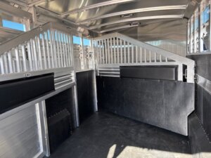 Interior of an empty 4+1 Trailer with partition panels, slatted walls, and a rubber-coated floor. Sunlight enters from the open side, and the surfaces of this well-maintained horse trailer appear clean throughout. -Stillwater Trailer Sales